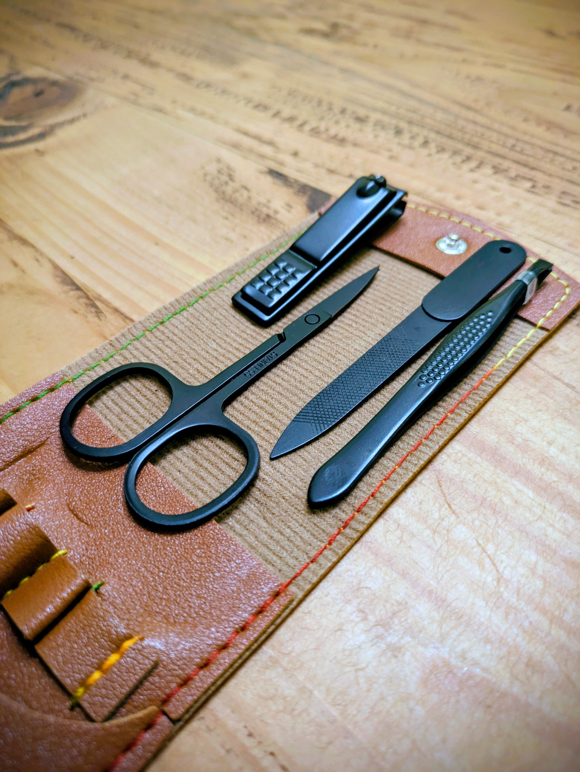 Angled view of black grooming tools in an open leather travel kit, showcasing scissors, clippers, file, and tweezers.