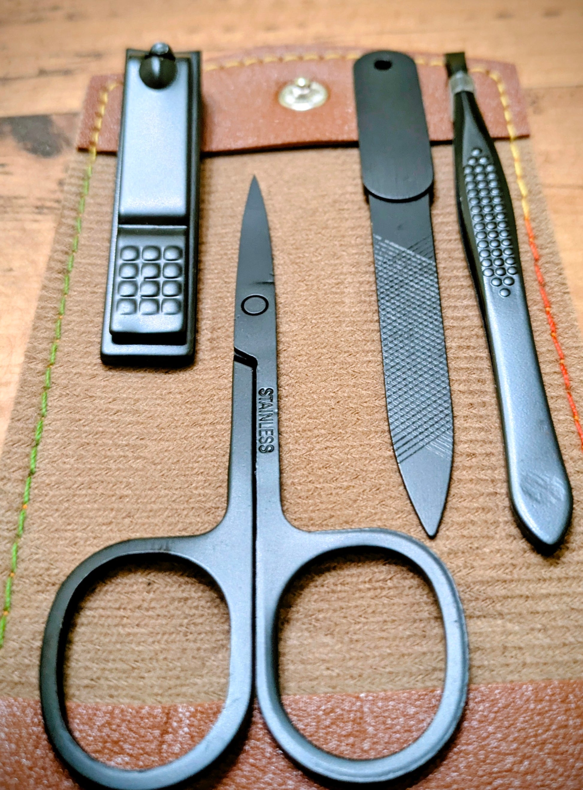 Close-up of black stainless steel grooming tools including scissors, nail clippers, file, and tweezers from the compact leather travel kit.