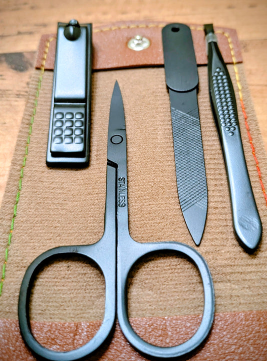 Close-up of black stainless steel grooming tools including scissors, nail clippers, file, and tweezers from the compact leather travel kit.